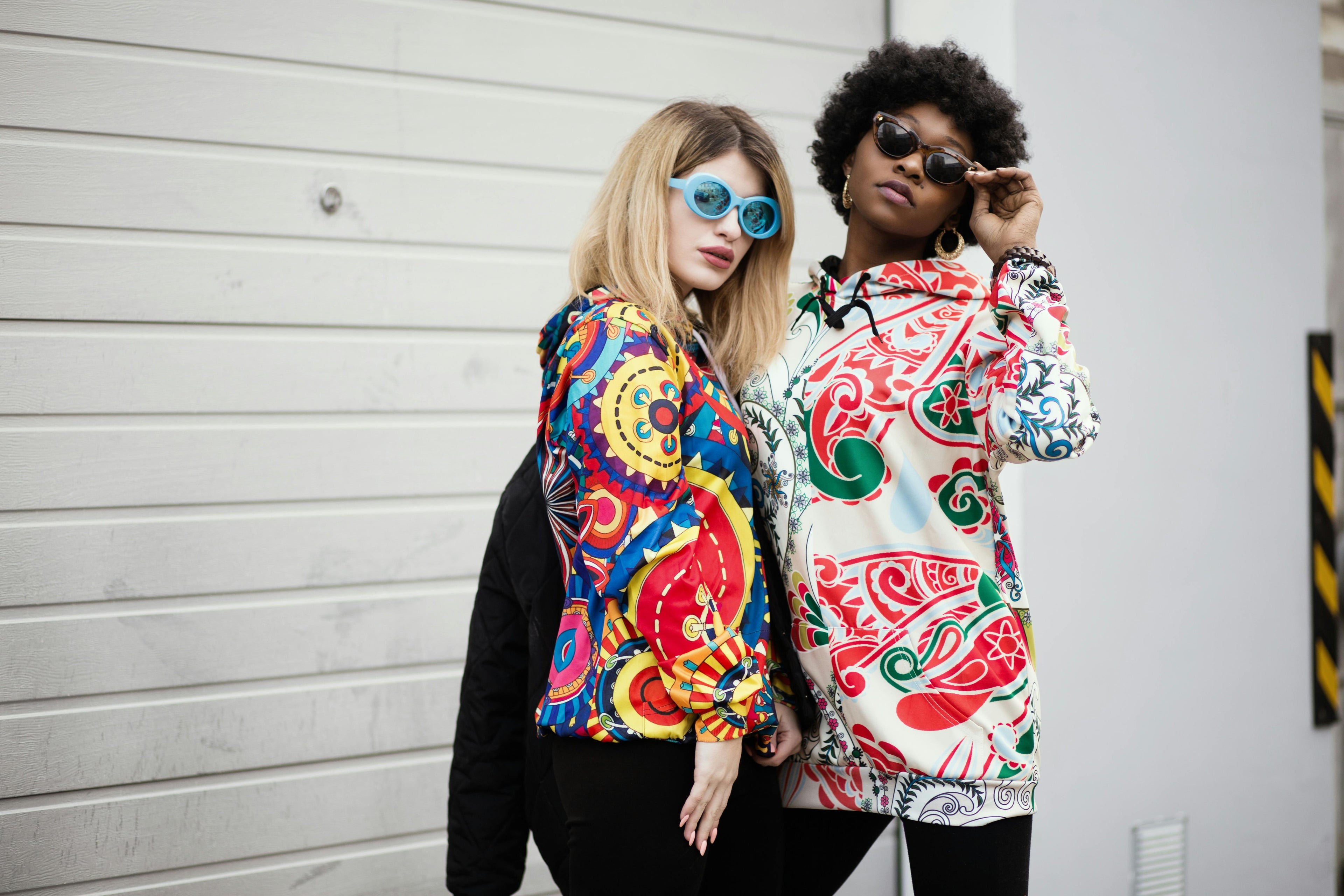 Two people wearing colorful patterned jackets standing against a plain background